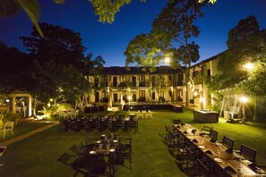 An outdoor dining area with tables and chairs, surrounded by a well-maintained lawn and trees. - Hotel Alakamanda (Anuradhapura)