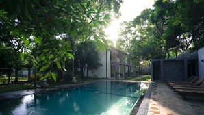 A swimming pool with a tiled deck, surrounded by trees and a building with a modern design. - Hotel Alakamanda (Anuradhapura)