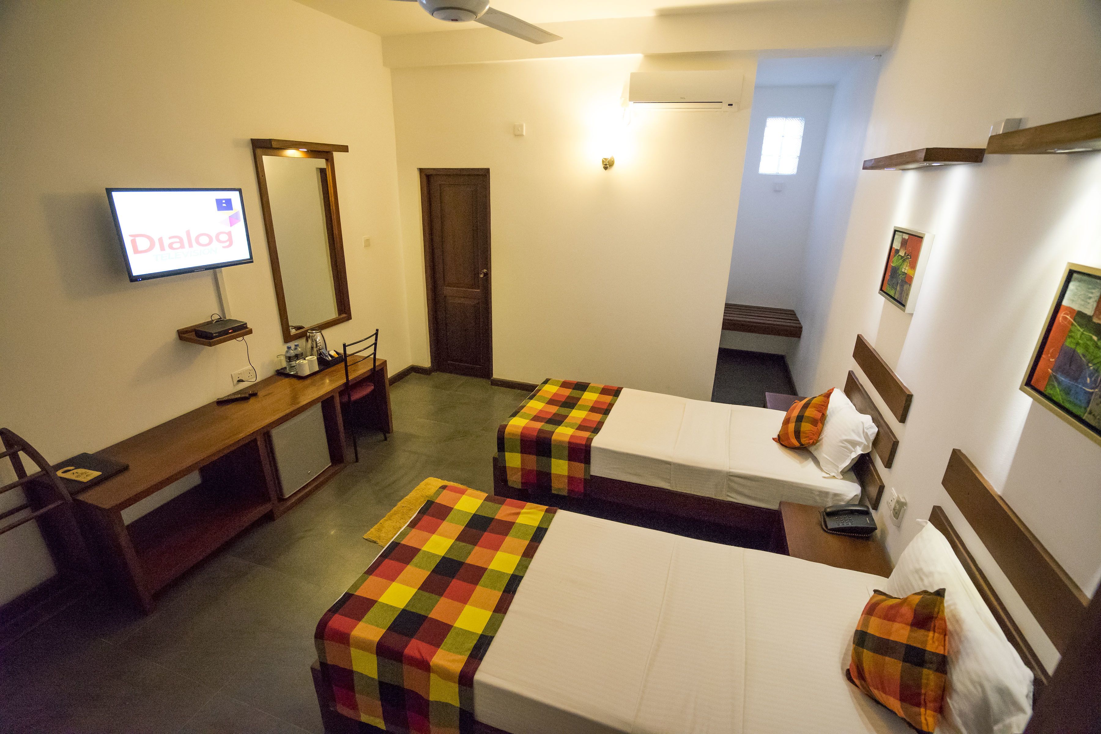 A hotel room with two single beds, a desk with a computer, a TV, and a mirror.