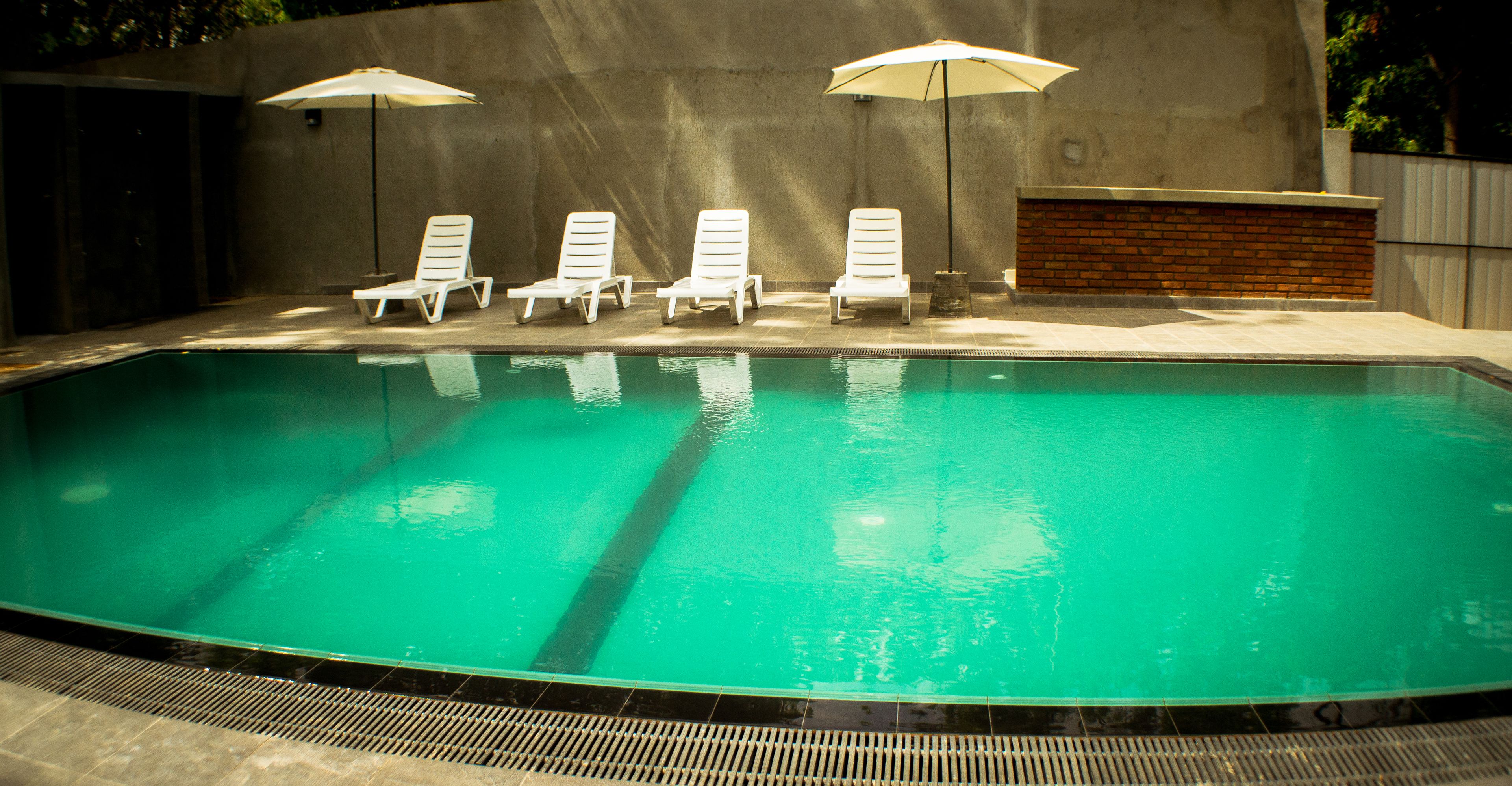 Une piscine avec quatre chaises longues blanches et deux parasols.