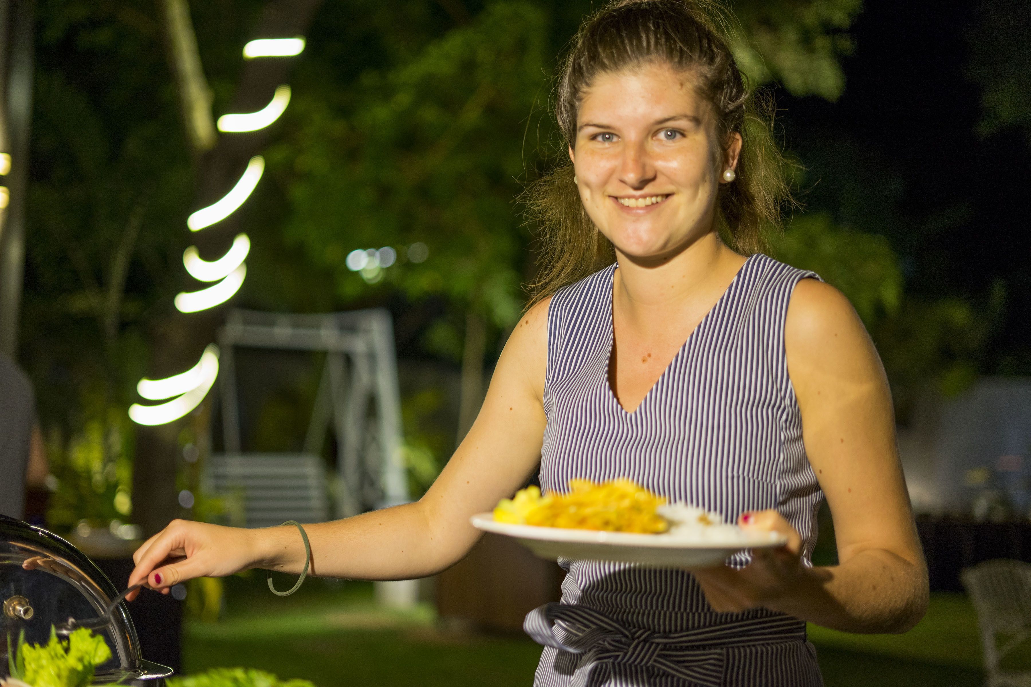 A person holding a plate of food outdoors at night.