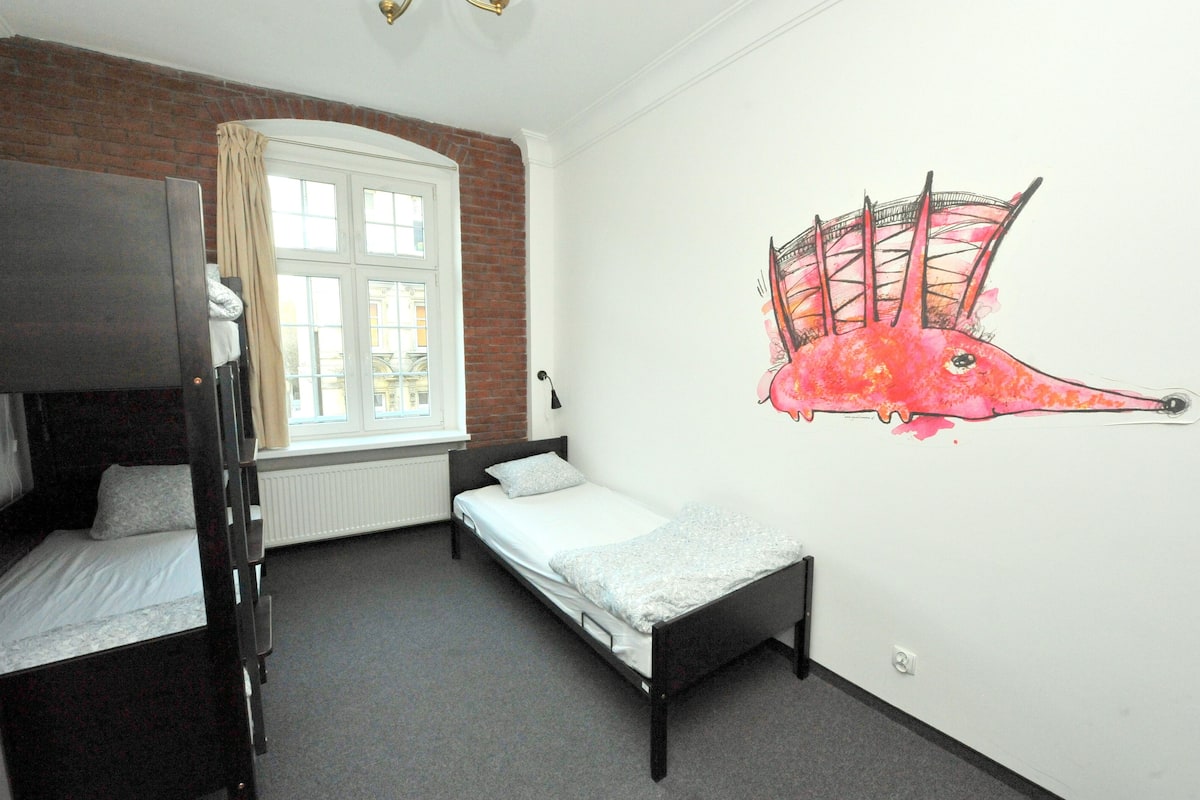 A room with a bunk bed, a single bed, a window with curtains, and a wall mural.