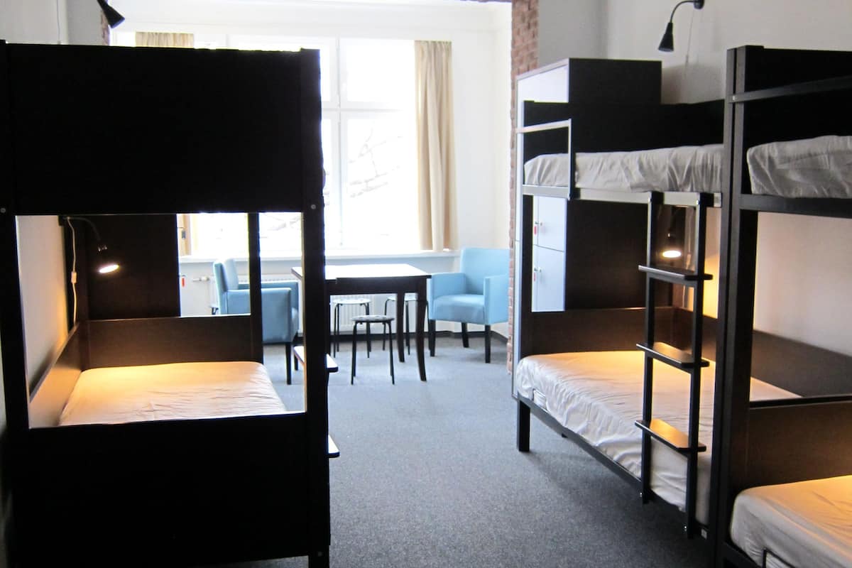 A dormitory room with bunk beds, a small table, and a chair.