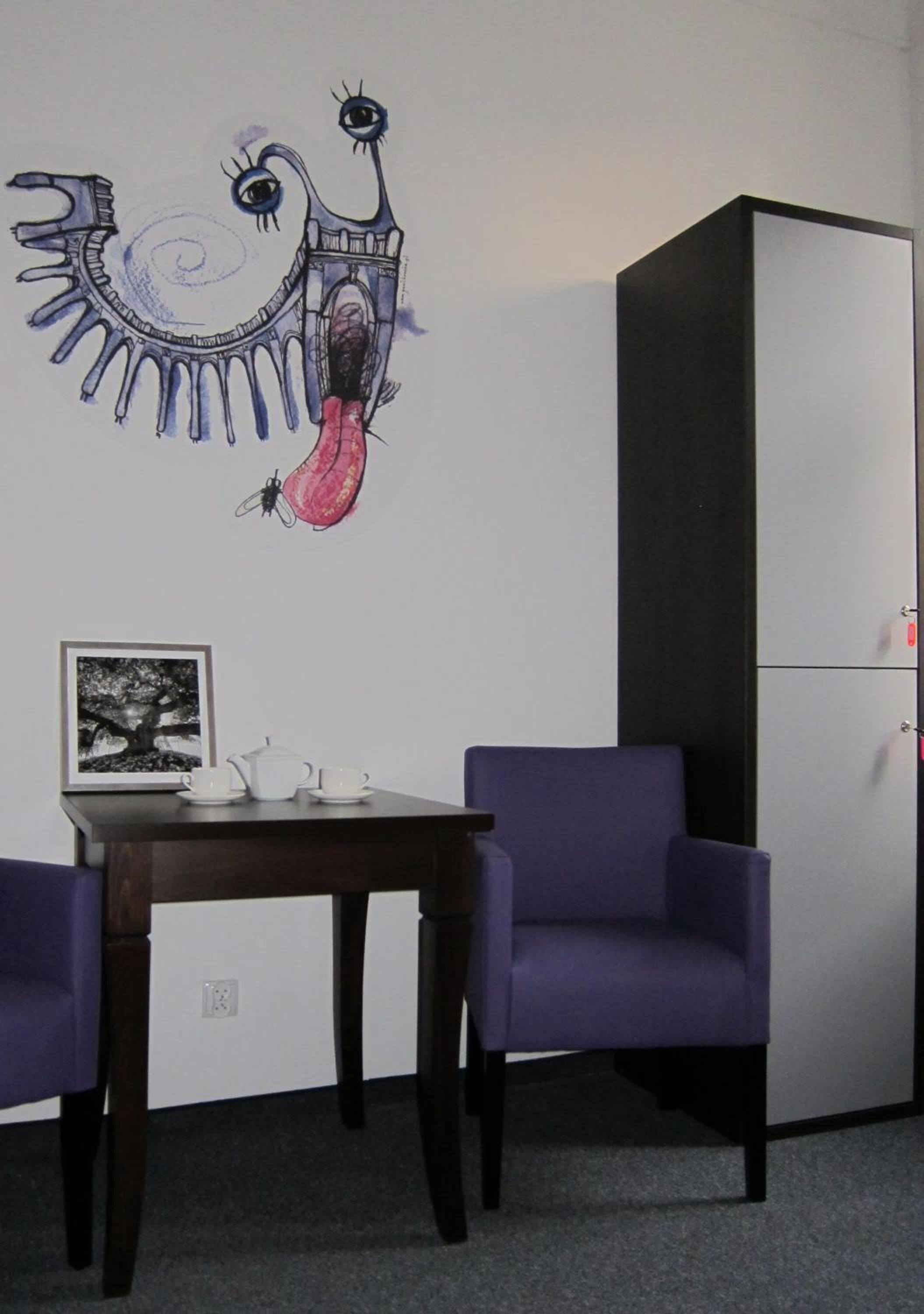 A room with a dining table, purple chairs, a white cabinet, and a wall with a unique mural.