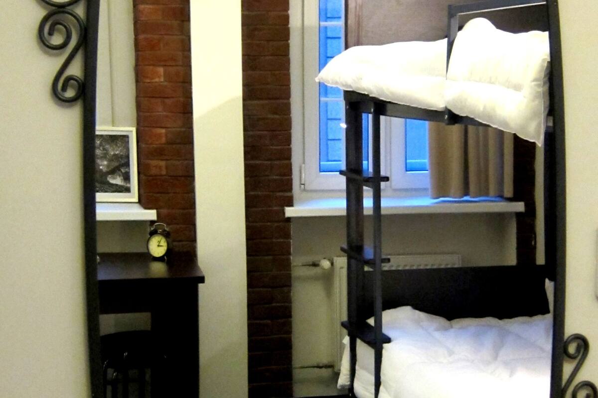 A room with a bunk bed, a small desk with a clock, and a window with curtains.