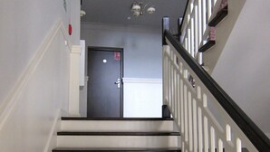 A staircase with white railings and dark steps, leading to a door with a fire exit sign. - Hostel Wratislavia (Wroclaw)