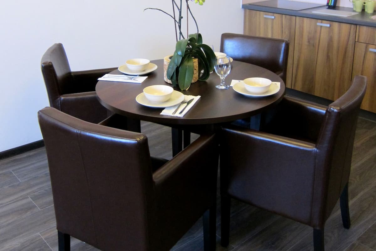 A dining area with a round table, four chairs, and a vase with flowers.