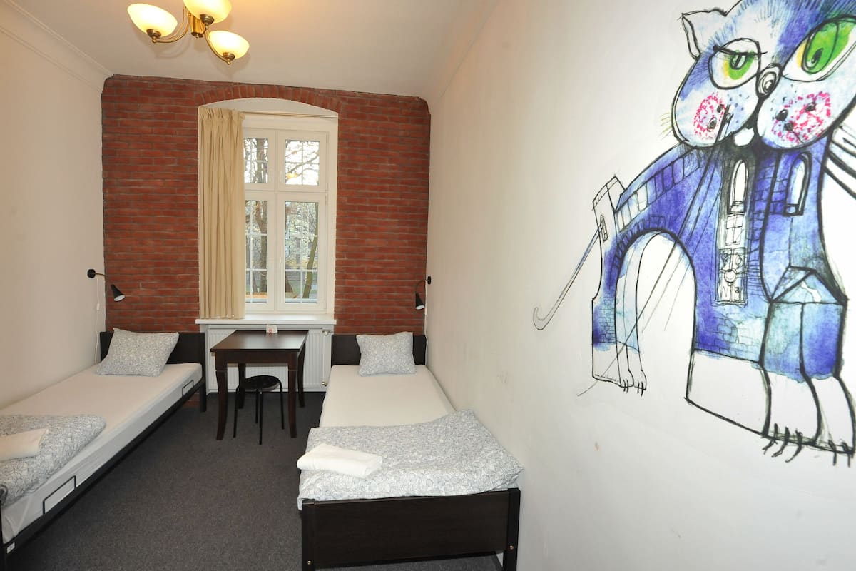 A dormitory room with two single beds, a desk, and a window.