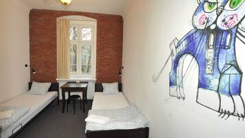 A dormitory room with two single beds, a desk, and a window.