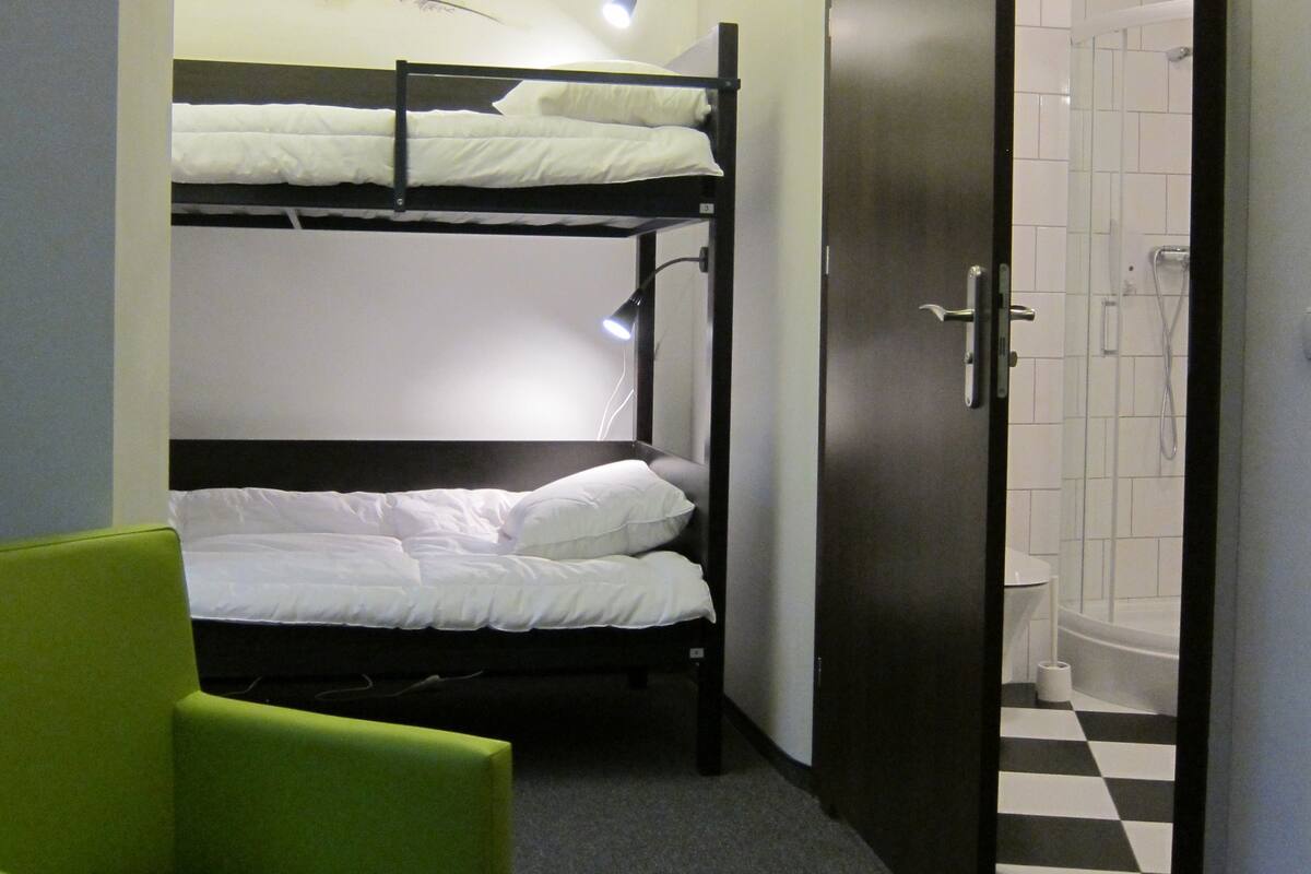 A dormitory room with bunk beds, a green chair, a shower area, and a wall mural.