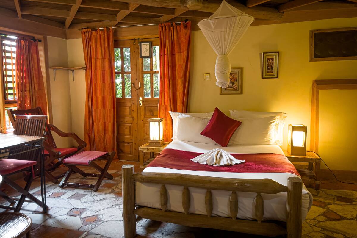 A wooden-framed bed with a red pillow, a bedside table with a lantern, and a window with orange curtains.