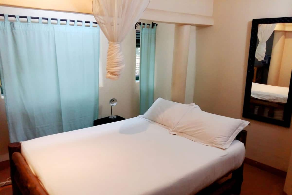 A bed with white bedding, a bedside table with a lamp, and a mirror on the wall.