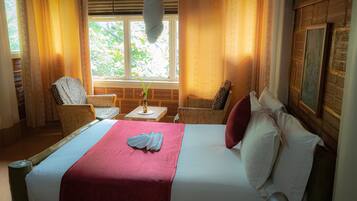 A hotel room with a bed, two chairs, a small table, and a window with curtains.