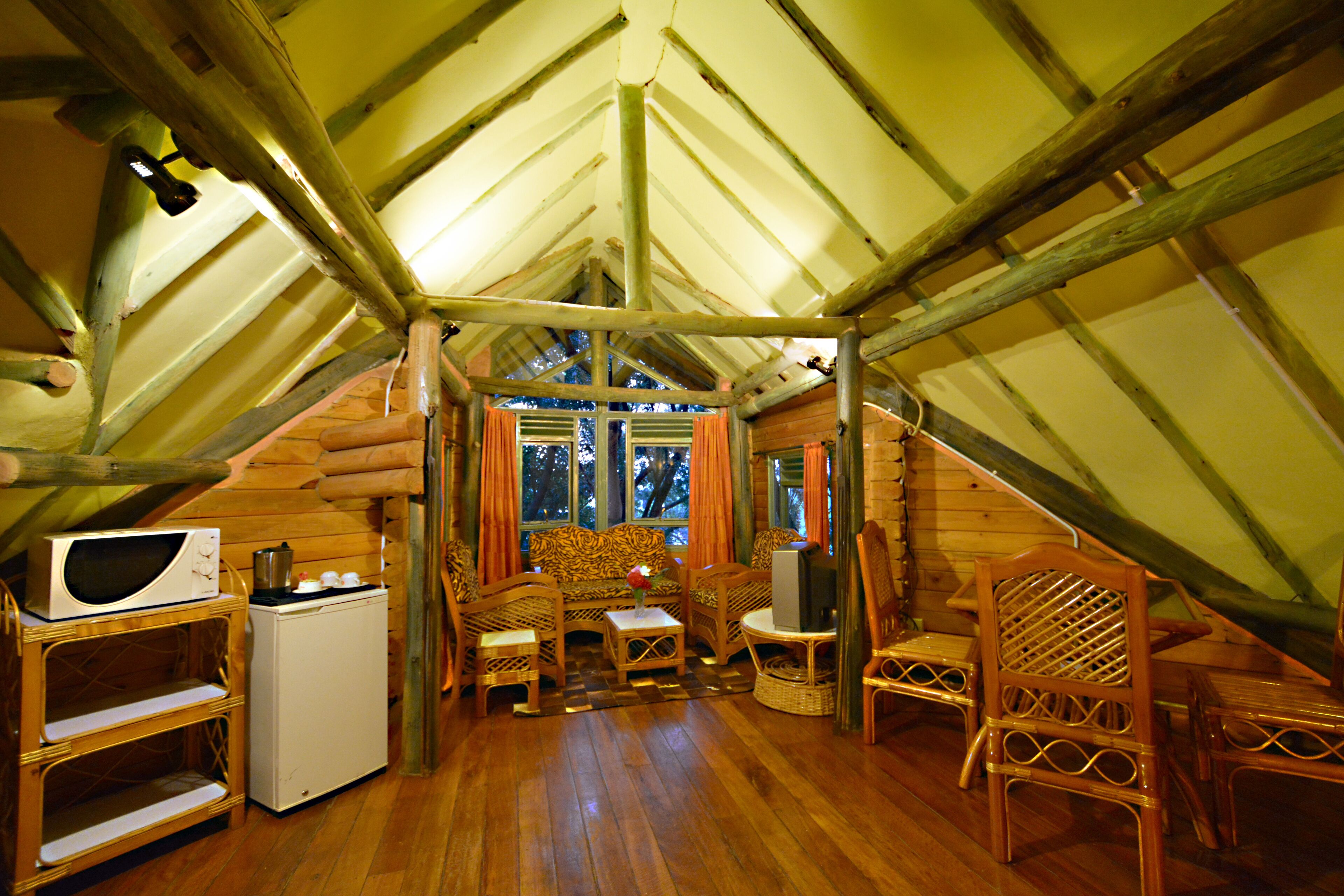 A cozy cabin interior with wooden walls, a ceiling fan, a small kitchenette, and a seating area with a sofa and chairs.