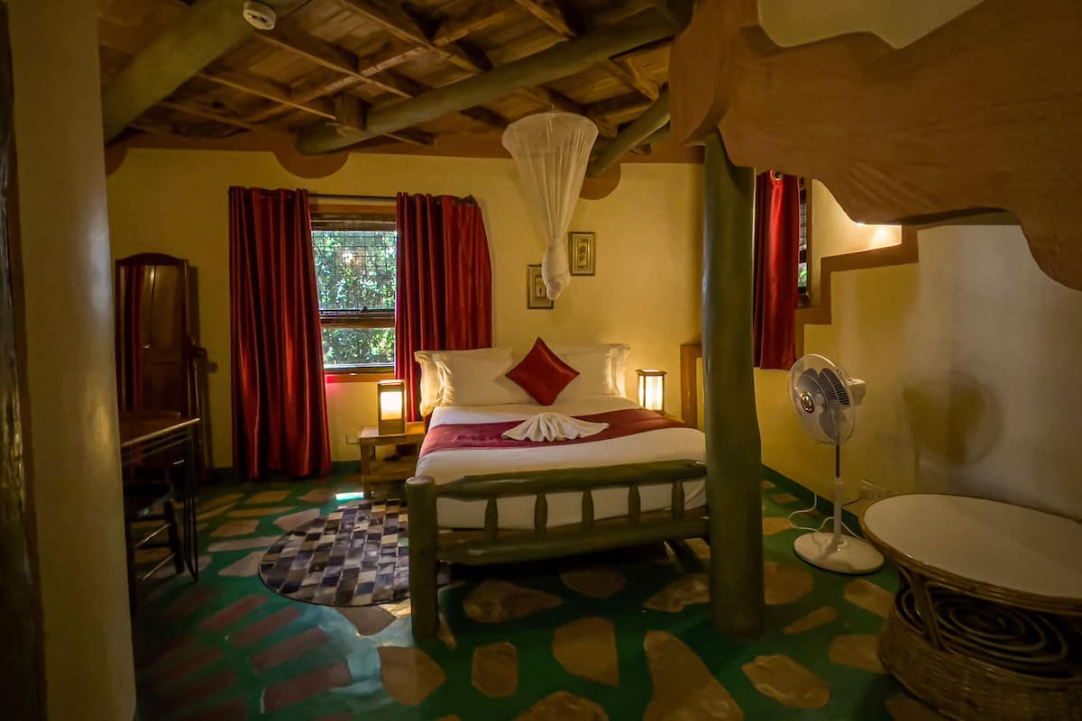 A room with a bed, a bedside table, a lamp, a fan, and a window with curtains.
