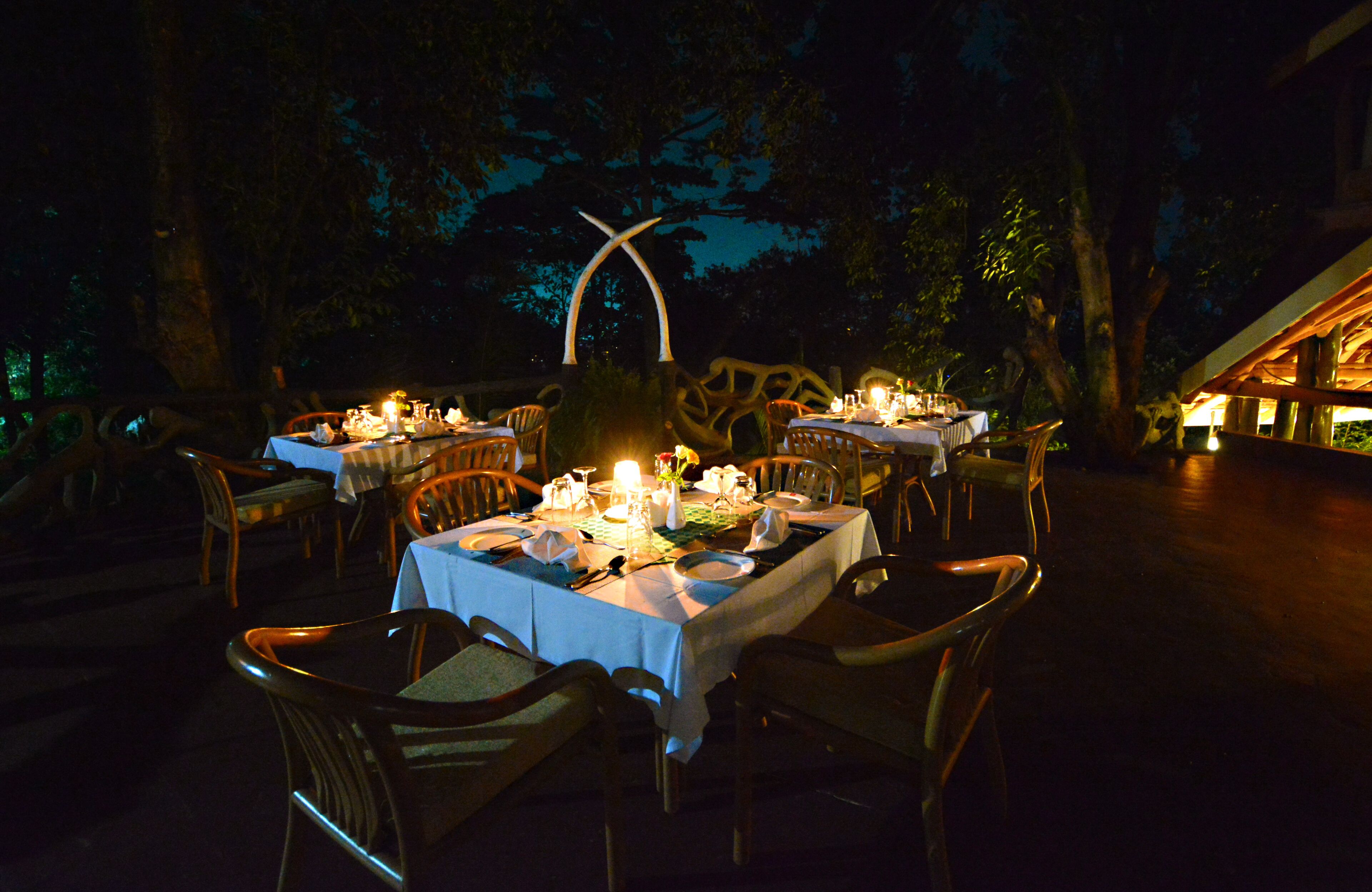 An outdoor dining area with tables set for a meal, surrounded by wooden chairs and a decorative archway.