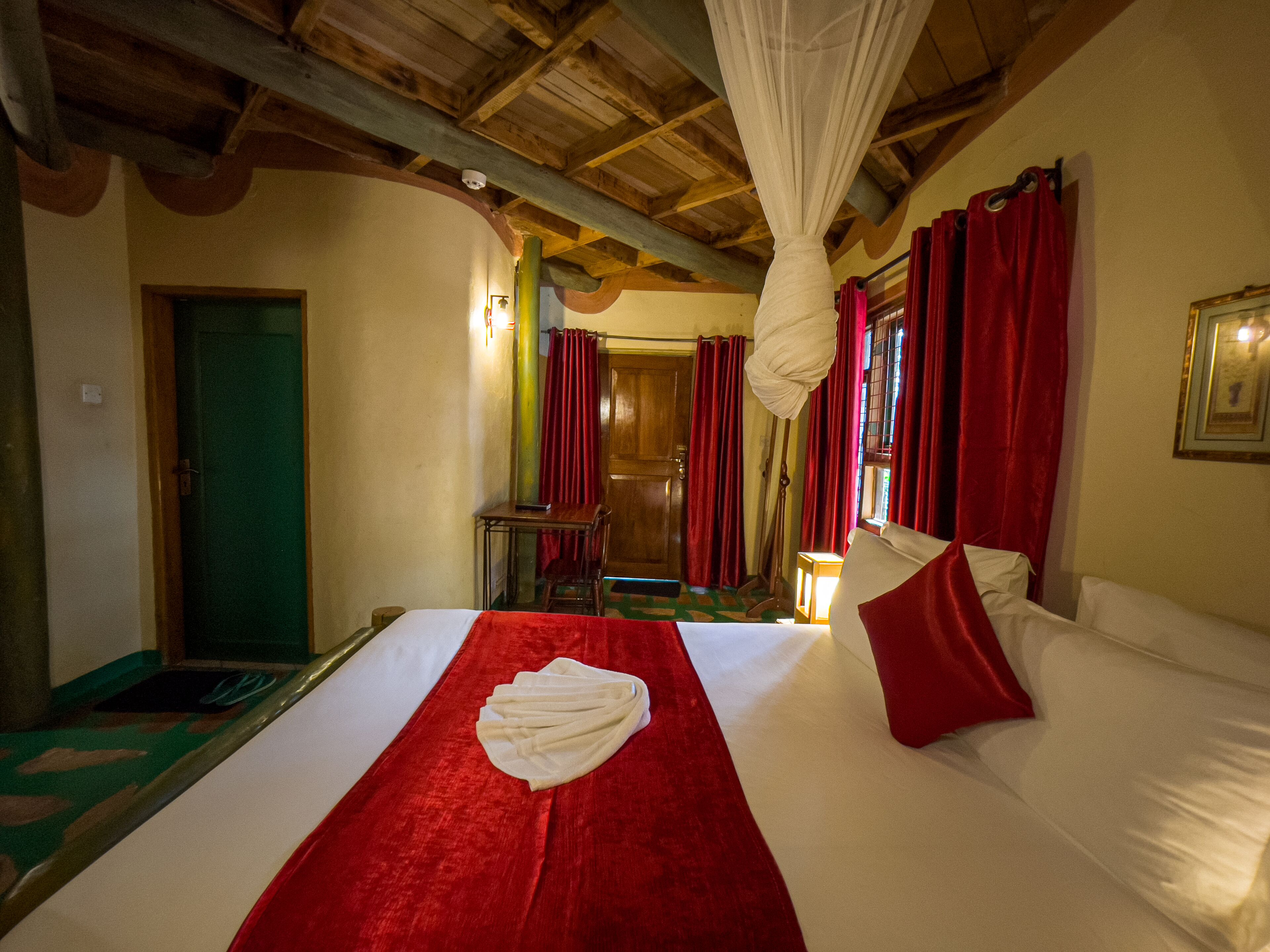 Ein Hotelzimmer mit einem Bett, roten Vorhängen, einer Holzbalkendecke und einer grünen Tür.