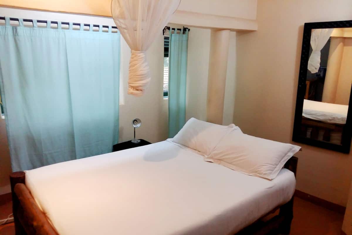 A bed with white bedding, a bedside table with a lamp, and a mirror on the wall.