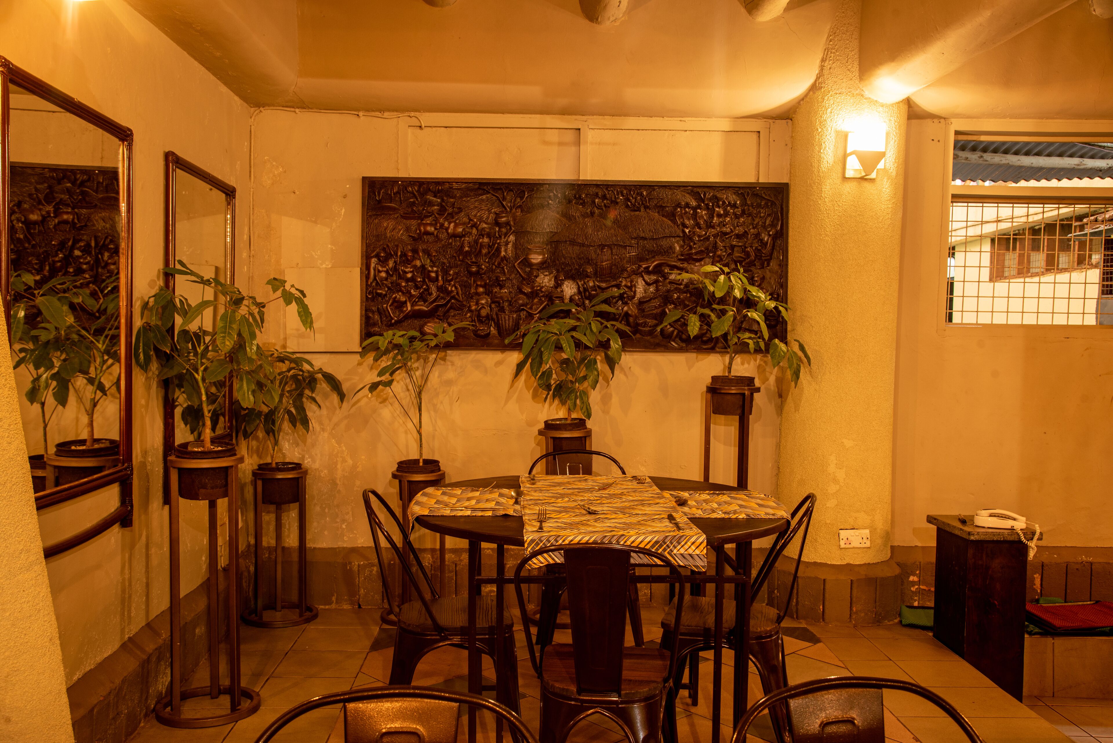 Un área de comedor con una mesa redonda, sillas, plantas en macetas y un mural grande en la pared.