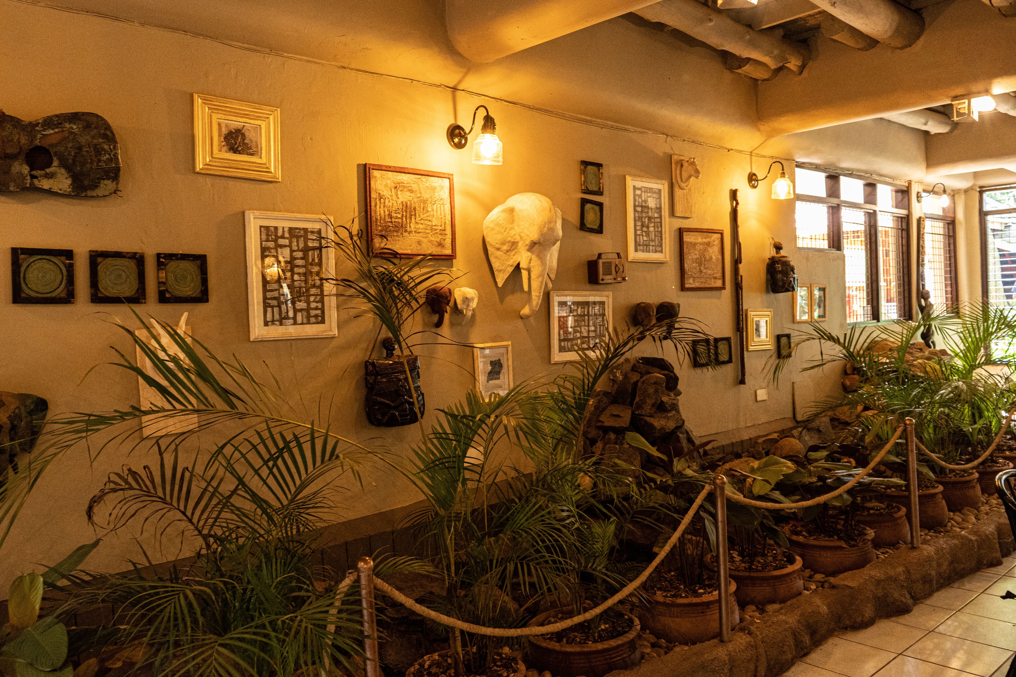 A room with a long wall decorated with framed pictures, a large white sculpture, and potted plants.