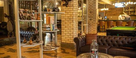 A bar area with a pool table, leather seating, and shelves with various items.