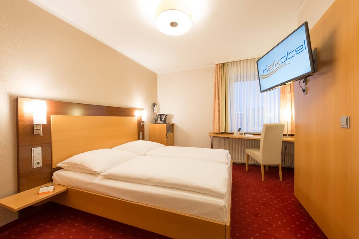 Quarto de hotel com cama, escrivaninha, cadeira, televisão e janela com cortinas.