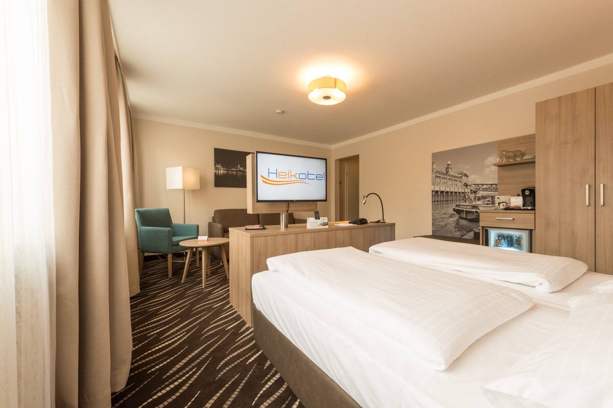 Quarto de hotel com duas camas, uma escrivaninha, uma cadeira, televisão e minibar.