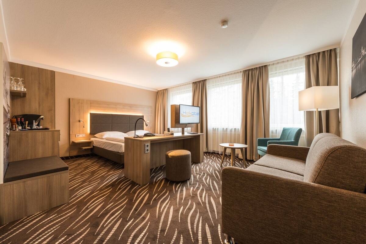 Quarto de hotel com cama, escrivaninha, cadeira e uma pequena mesa.