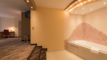 Ein Hotelbad mit einer großen Badewanne, einer Duschkabine und einer Sitzecke mit einem gemusterten Teppich.