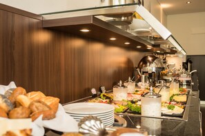 A buffet setup with various food items and beverages, including bread, salads, and hot dishes, in a modern kitchen setting. - Heikotel Hotel Windsor (Hamburg)