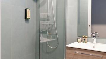 Un baño moderno con ducha de vidrio, tocador de madera con espejo y un estante pequeño con artículos de aseo.