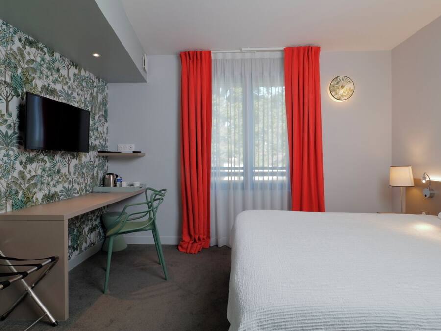 Une chambre d’hôtel avec un lit, un bureau et une chaise, une télévision et une fenêtre avec des rideaux rouges.
