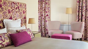 Une chambre d’hôtel avec un lit, deux chaises, un banc et des rideaux à motifs floraux.