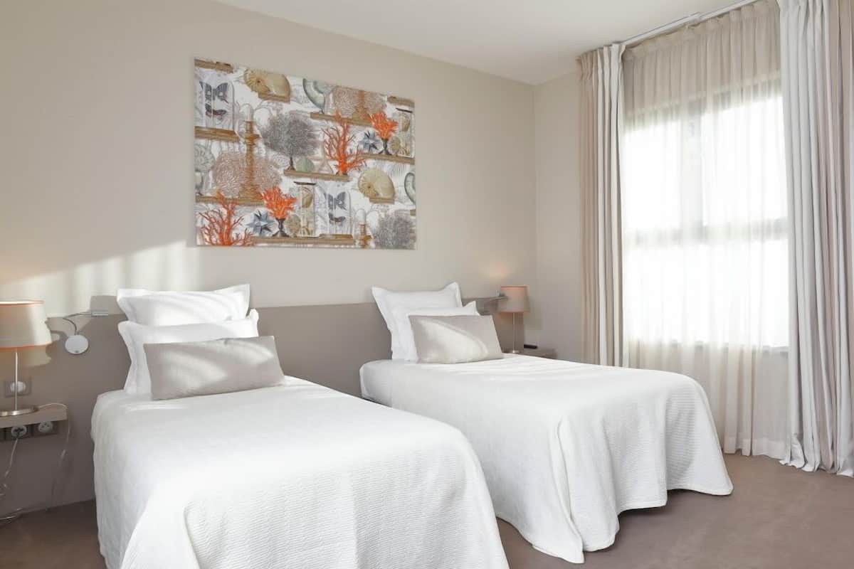 Habitación de hotel con dos camas, un cuadro abstracto grande en la pared y una ventana con cortinas translúcidas.