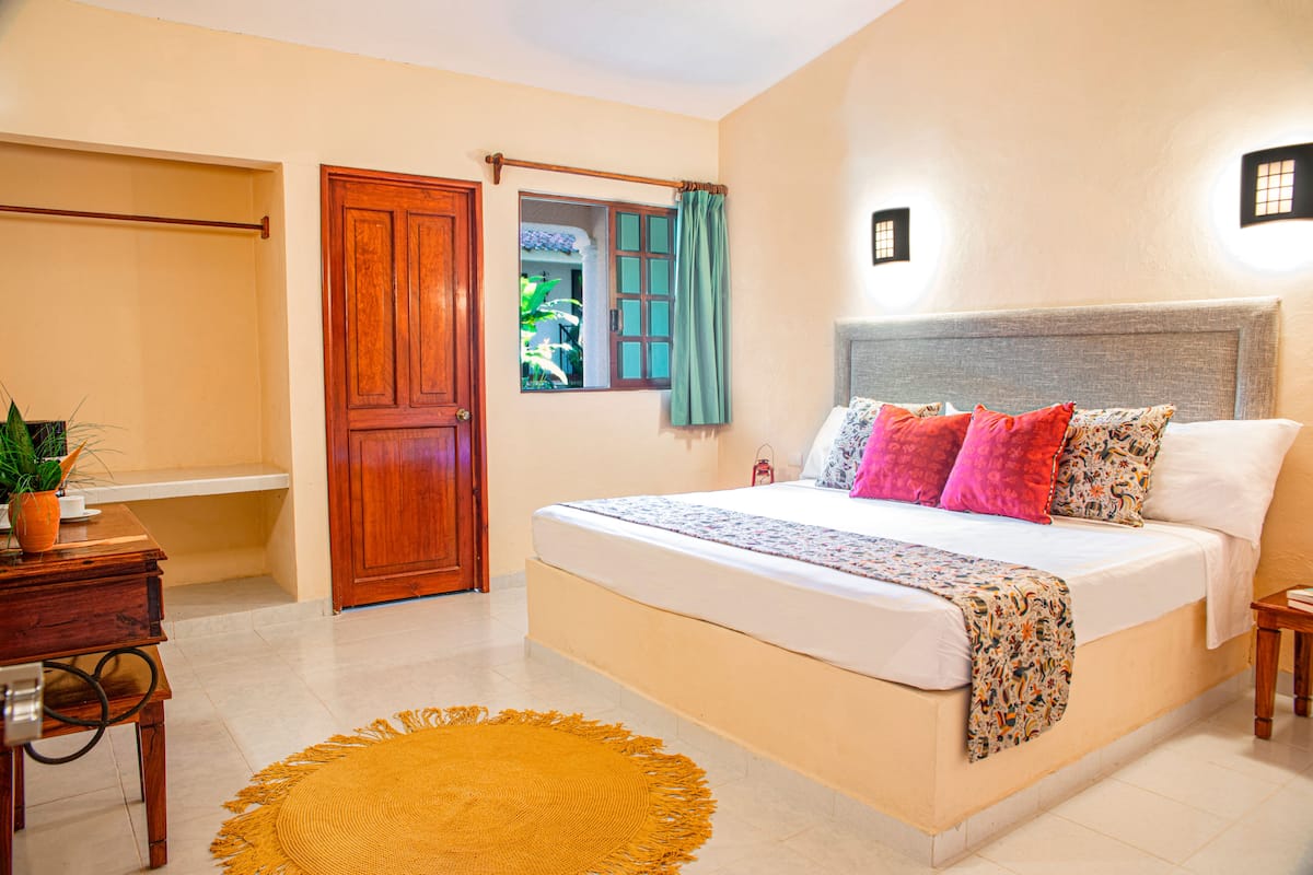 A bedroom with a bed, wooden furniture, a window with curtains, and a small table.