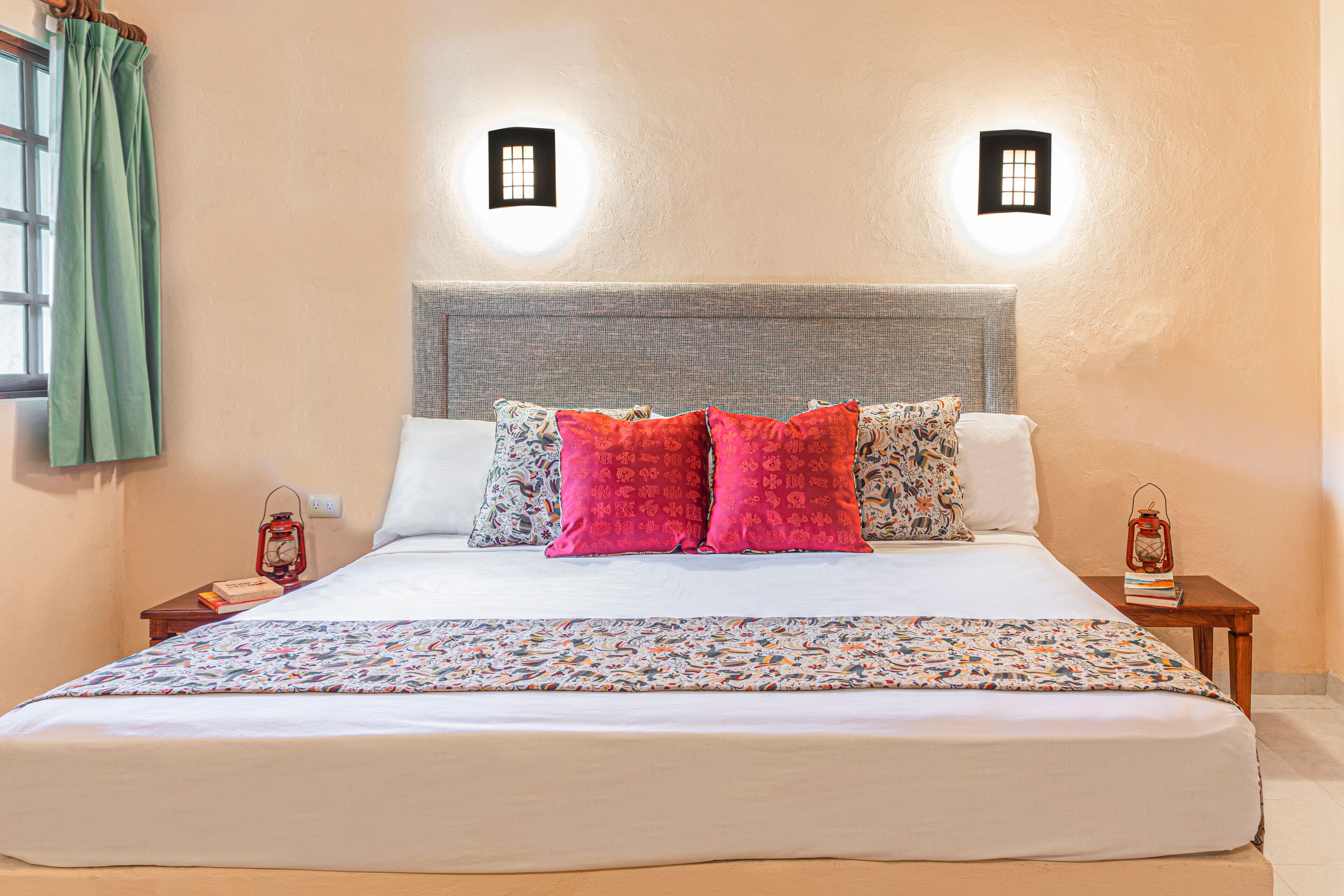 A neatly made bed with patterned bedding, two bedside tables with lanterns, and a window with curtains.