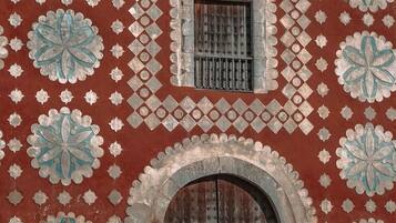 Fachada de edificio con intrincados diseños geométricos y florales, un amplio arco de entrada y un pequeño ventanal con rejas.