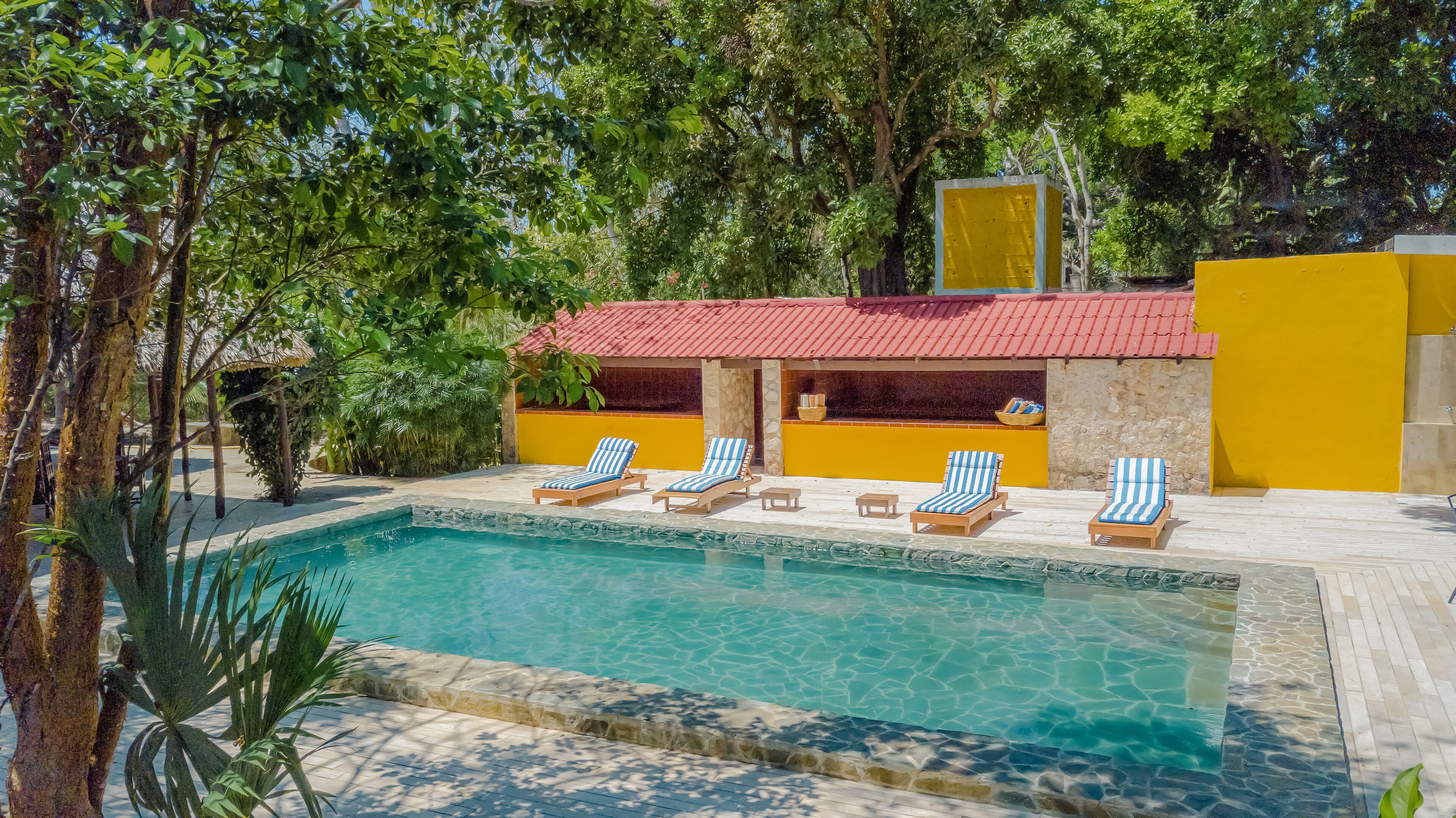 A pool area with lounge chairs and a building with a red roof.