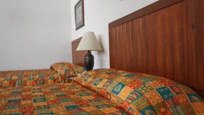 A room with two beds, wooden headboards, a lamp, and a patterned bedspread. - Hotel Fiesta Versalles (Monterrey)