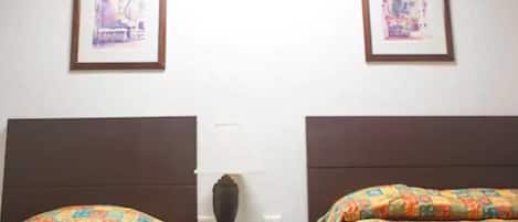 A hotel room with two beds, each with colorful bedding. There are framed pictures on the wall above the beds.