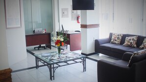 A modern living room with a glass coffee table, a sofa with patterned cushions, and a flat-screen TV mounted on the wall. - Hotel Fiesta Versalles (Monterrey)