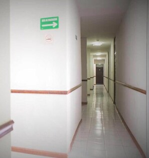 Un long couloir étroit, avec un panneau de signalisation vert sur le mur de gauche et un panneau « interdiction de fumer » au-dessus.