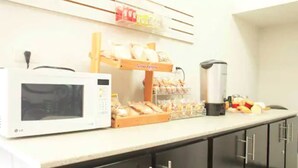 A kitchen area with a microwave, bread display, and coffee maker. - Hotel Fiesta Versalles (Monterrey)