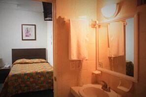 Ein Hotelzimmer mit einem Bett, einem Badezimmer mit Waschbecken und Spiegel sowie einem gerahmten Bild an der Wand.