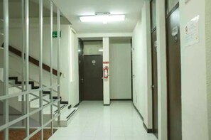 Un couloir avec un escalier sur la gauche, un extincteur fixé au mur et une porte au fond.