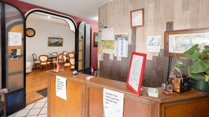 Un espace d’accueil d’hôtel avec un comptoir en bois, des chaises, une horloge et divers avis affichés au mur.