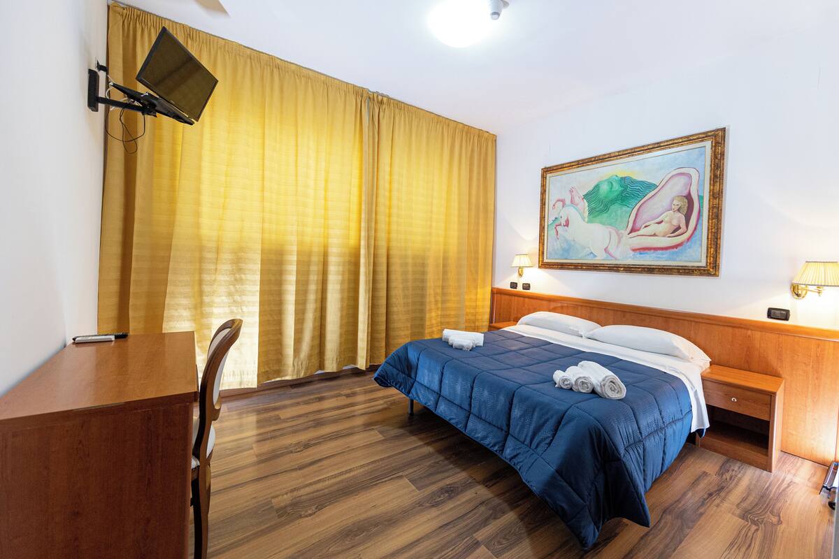 Une chambre d’hôtel avec un lit, un bureau, une chaise et un tableau au mur.