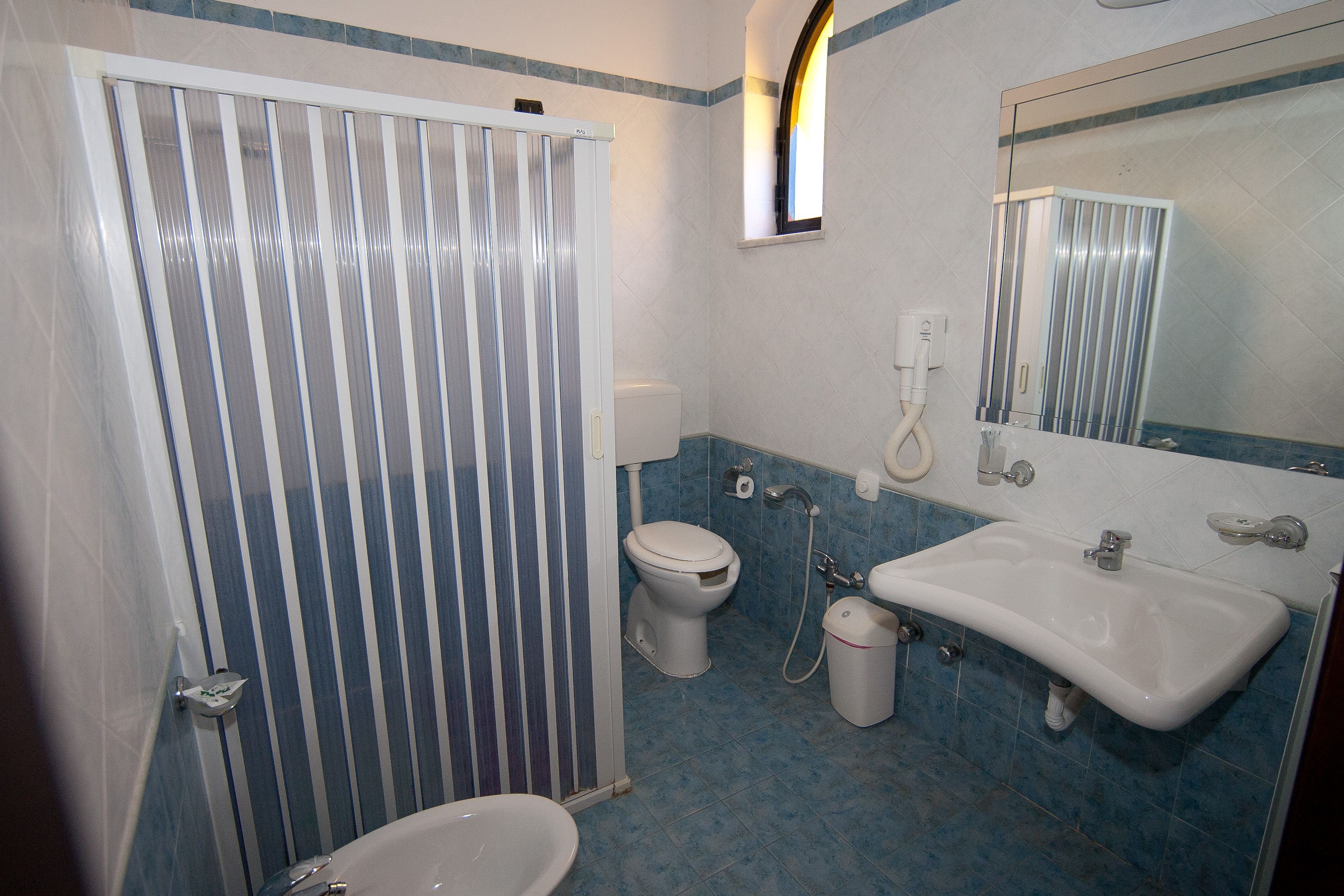 A bathroom with a shower, toilet, sink, and mirror.