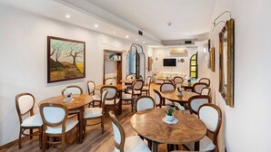 Un espace repas avec plusieurs tables rondes et des chaises, un tableau au mur et un téléviseur en arrière-plan.