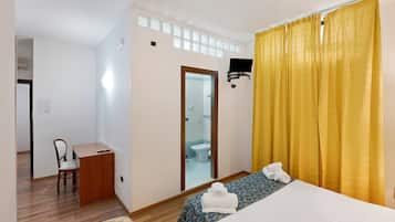 A hotel room with a bed, a desk, a chair, a bathroom visible through a door, and yellow curtains.